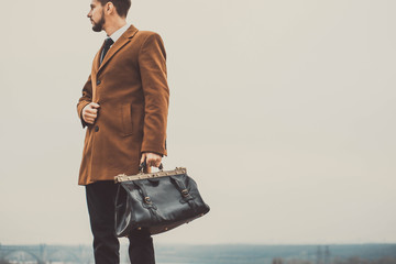 Portrait of a thirty years old bearded guy, in a business style, with a leather bag in his hands....