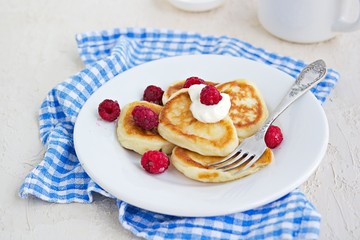 Breakfast, pancakes with sour cream and raspberries on a white plate on a light concrete background. Child's breakfast in front of the school. School breakfast concept.