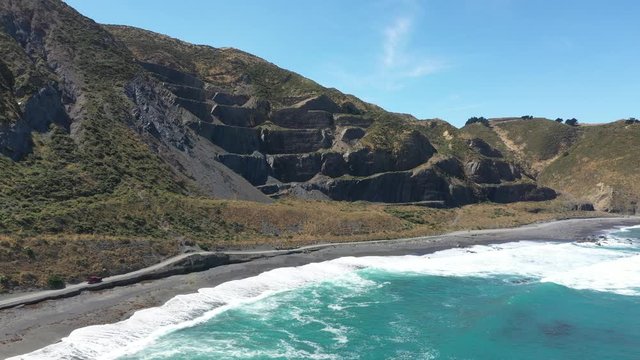 Aerial footage of car riding on black sand road by the beach and mountains in Wellington, New Zealand