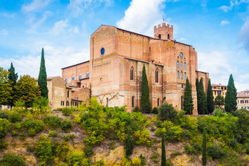 Fototapeta na wymiar Medieval basilica di San Domenico, Siena, Tuscany, Italy. Red stone, green trees, blue sky with white clouds. Pictorial tuscan cityscape.