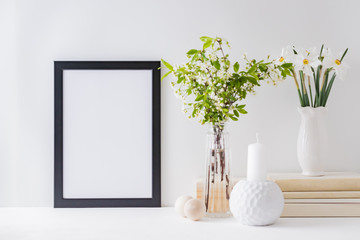 Home interior with decor elements. Mockup with a black frame, spring flowers in a vase on a light background
