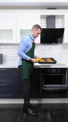 vertical image. handsome man in tie and apron pulls pies out of the oven