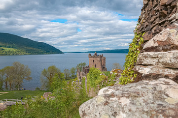 Fototapeta na wymiar Stone wall with the ruins of Urquhart Castle and Loch Ness behind. Concept: Scottish historic sites, archaeological sites, Scottish nature colors