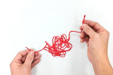 Two hands untangling a tangled red yarn in white background top view. Problem solving skills.