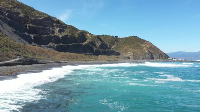 Aerial footage of drone zooming out mountain over black sand beach in Wellington, New Zealand