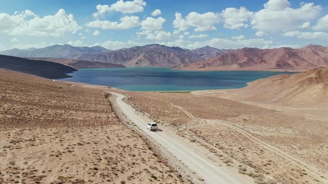Aerial over off road 4x4 car driving along gravel trail path toward lake in arid mountains.Pamir Highway silk road travelling adventure in Tajikistan,Asia.Khorugh Bulunkul lake. 4k drone flight video