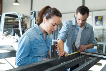 man and woman measuring length of metal in workshop