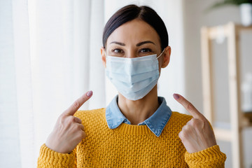 Portrait of young Asian woman,  wearing a medical surgical disposable face mask to prevent...