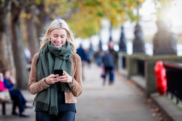Eine attraktive, blonde Frau läuft auf der Straße und liest ihre Emails und Nachrichten auf dem...
