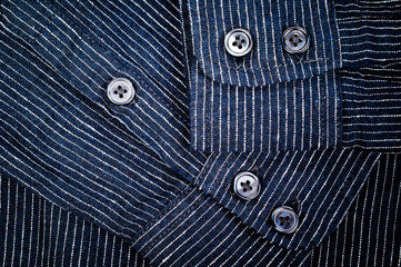 The texture of a denim shirt in dark blue with a small strip on the buttons. Background for fabric and clothes. Fashion, style and practicality.