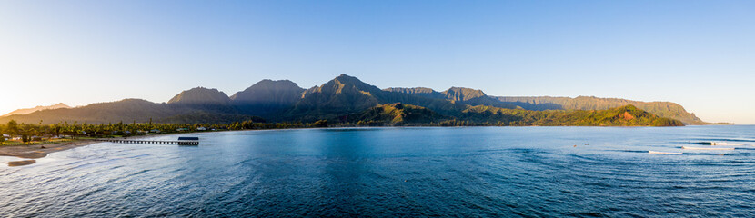 Aerial panoramic image at sunrise off the coast over Hanalei Bay and pier on Hawaiian island of...