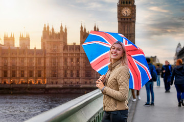 Eine blonde Touristin hält  einen Souvenir Regenschirm mit Britischer Flagge vor dem Big Ben Turm in London während eines Städtetrips