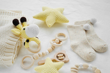 Knitted toy giraffe, yellow stars and wooden teether for newborn on white bed.  Gender neutral ...