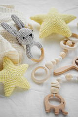 Knitted toy bunny, yellow stars and wooden teether for newborn on white bed.  Baby stuff and...
