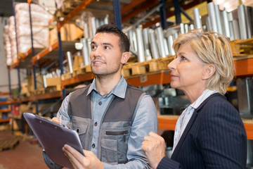 worker with clipboard and businesswoman in warehouse