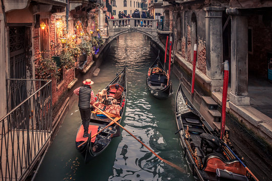 Gondolier rowing down a narrow canal in venice with christmas lights illuminating his gondola