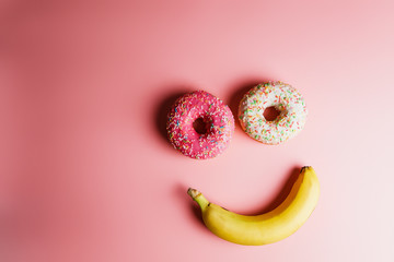  funny smiley of two donuts and banana on a pink background with place for text, an example of junk...