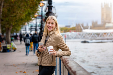 Portrait einer moderne, jungen Stadtfrau mit Handy und Kaffee in der hand am Ufer der Themse in...