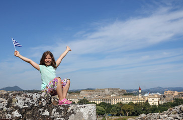 happy little girl with hands up and greek flag at Corfu fortress