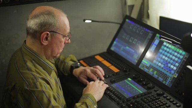 Man illuminator operator at the control panel programs the stage lighting for the show