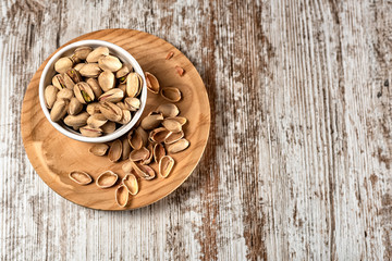 Pistachio nuts in white bowl on an old wooden table, Top view. Space for text
