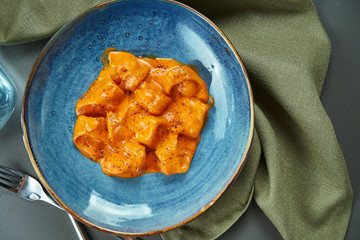 Appetizing orange ravioli in a sauce with different fillings (meat, fish) in a blue bowl on a wooden background. Italian cuisine. Top view, flat lay, Copy space