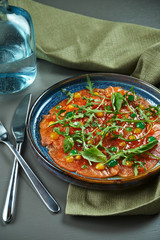 Luxury salad of slightly salted crudo salmon with arugula and sauces in a blue plate on a wooden background. Antipasti seafood. Close up, selective focus