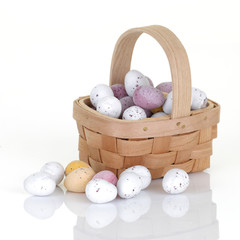 Wood basket of small easter egg candy on white with reflection