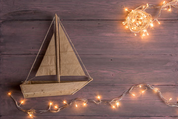 Travel and adventure creative concept - toy boat on a wooden background. Christmas lights as a sea waves