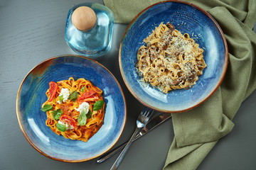 Two fresh, homemade pasta with wild mushrooms and bolognese with tomatoes in a blue bowl on a wooden background. Top view, flat lay