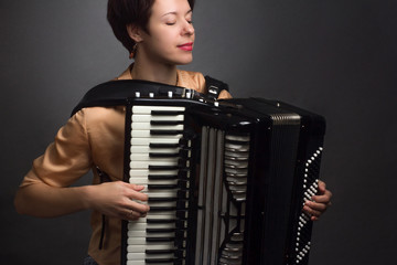 A brunette in a gold shirt, with short haircut, on a light gray background of the Studio. With accordion musician