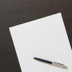 Template of white paper with pen on dark wenge color wooden background.
