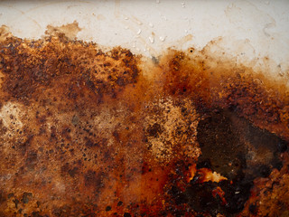 Rusty metal surface with wet rust with smudges of water and drops. Brown, black and yellow rust and dirt on white enamel. Rusted brown and white abstract texture. Corroded metal background.