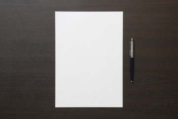 Template of white paper with pen on dark wenge color wooden background.