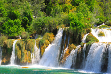 Fototapeta na wymiar A picturesque cascade waterfall among large stones in the Krka Landscape Park, Croatia in spring or summer. The big beautiful Croatian waterfalls, mountains and nature.