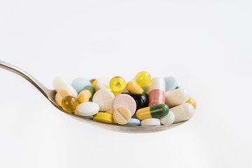 Assorted pharmaceutical medicine pills, tablets and capsules in a spoon on white background. Healthcare concept.
