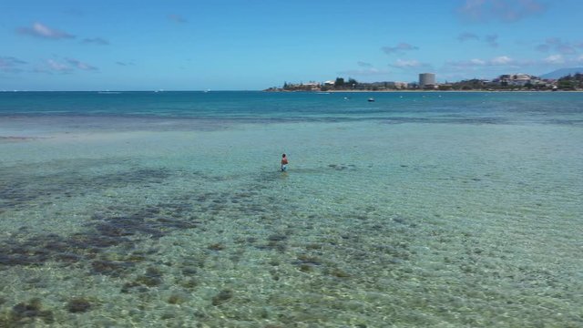 Drone circling over a man walking in a low tide beach in Noumea, New Caledonia