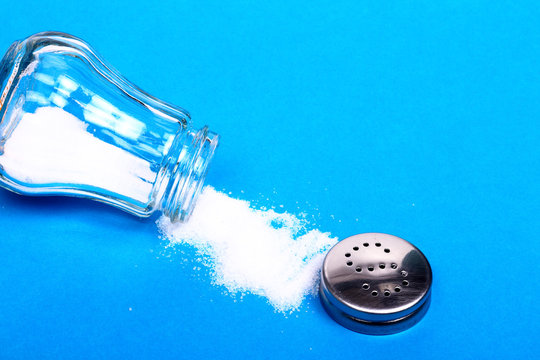 Salt spilling out from a glass sat shaker isolated on a blue background with copy space