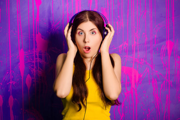 Portrait of a young, beautiful woman with long hair listening to music on headphones. Studio photo on abstract, purple background.