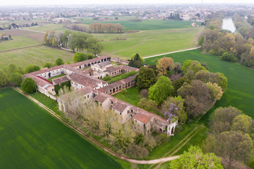 Aerial view of a green plain with an ancient, abandoned monastery surrounded by trees in the foreground