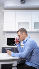 vertical shot, man is resting in the kitchen with a glass of wine uses a smartphone
