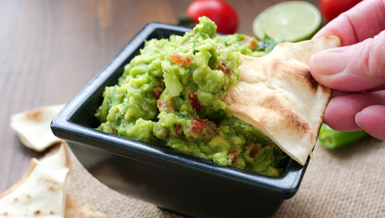 Hand dipping wheat tortilla chips into a bowl of freshly made guacamole