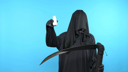 A man in a death suit with a scythe, shows a bottle of drink. blue background