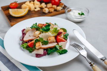 Fresh Caesar salad with delicious chicken breast, spinach, cabbage, arugula, Parmesan and cherry tomatoes on a light background. Caesar sauce, lemon, broken cheese. The concept of healthy and dietary 