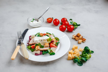 Fresh Caesar salad with delicious chicken breast, spinach, cabbage, arugula, Parmesan and cherry tomatoes on a light background. Caesar sauce, lemon, broken cheese. The concept of healthy and dietary 