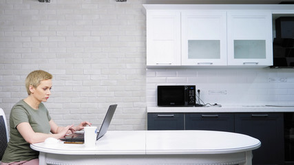 a woman uses a laptop sitting on the kitchen table, she is happy