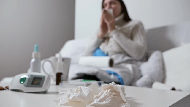 Healthcare and medical concept.Young sick woman sneezing at home at night on the couch. Girl runny nose and holding tissue, flu symptoms