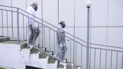 people walk past technological buildings in protective suits and respirators