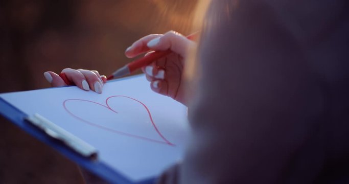 woman drawing heart symbol at clipboard