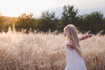 girl with open hands enjoying rural magic atmosphere among golden fields in the countryside